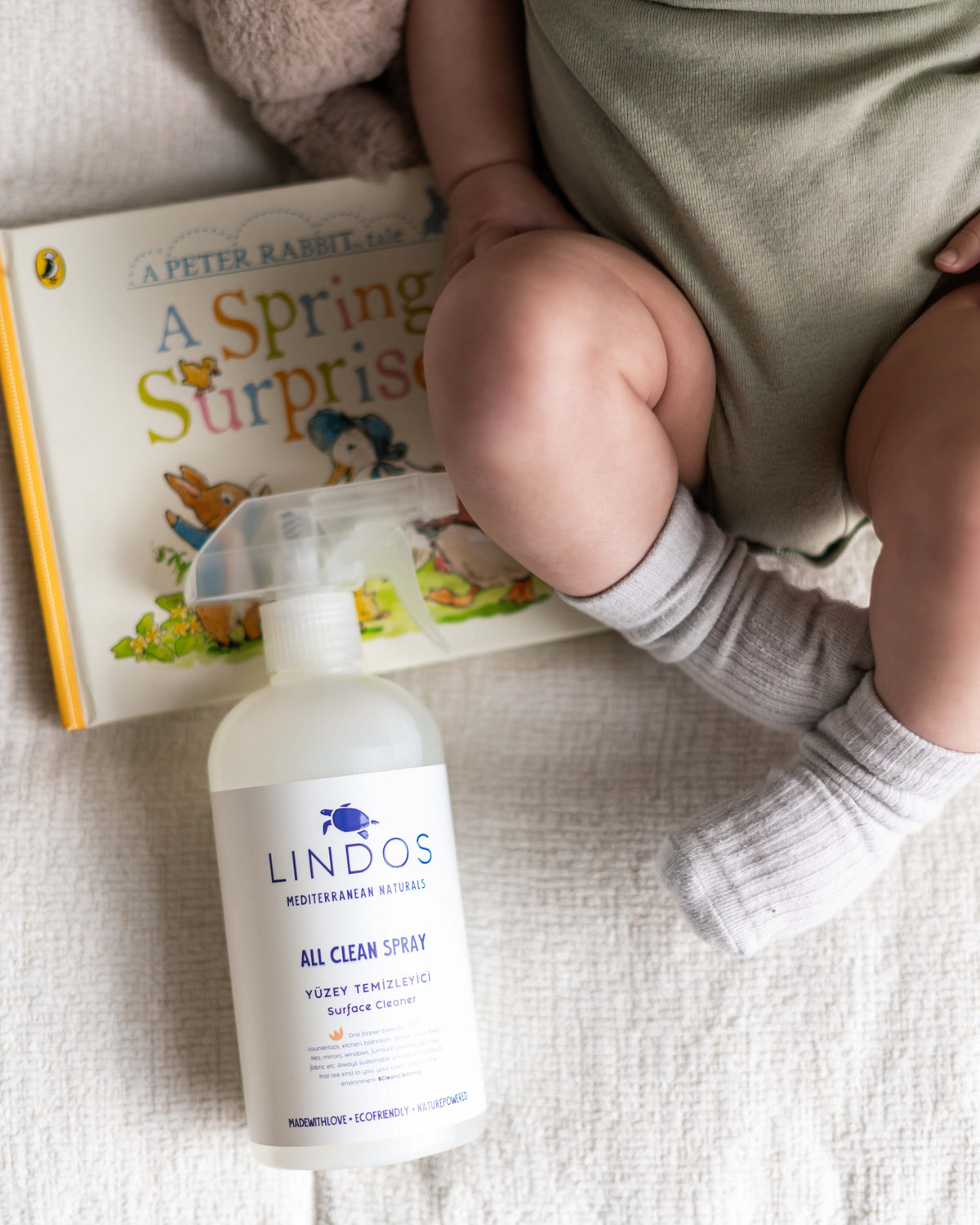 Lindos All Clean yüzey temizleyici spreyi, bebek odasında bir çocuk kitabının ve bebeğin ayaklarının yanında.